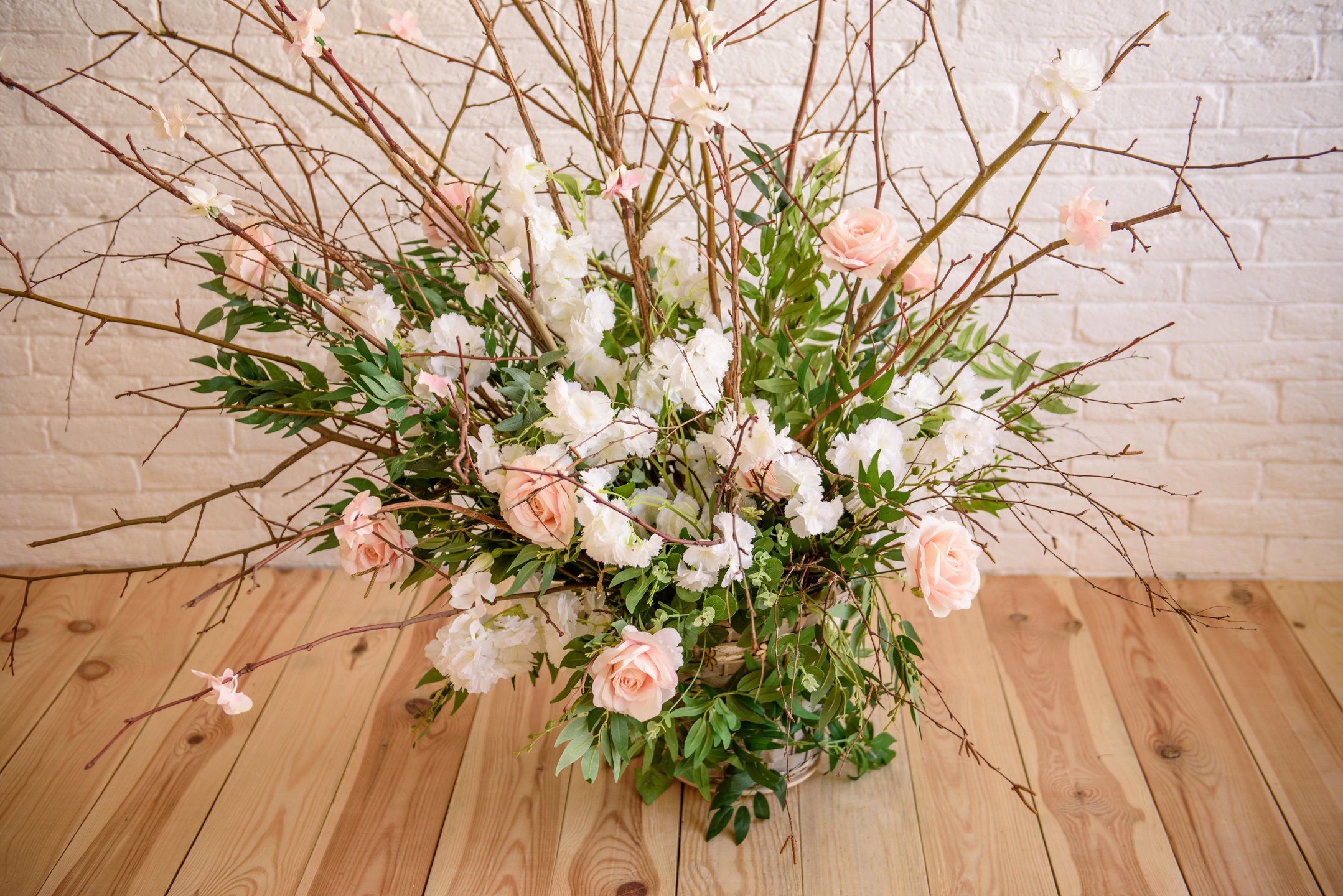 Decorations of Branches with Beautiful Pink and White Flowers in the Basket against the Background of a White Brick Wall